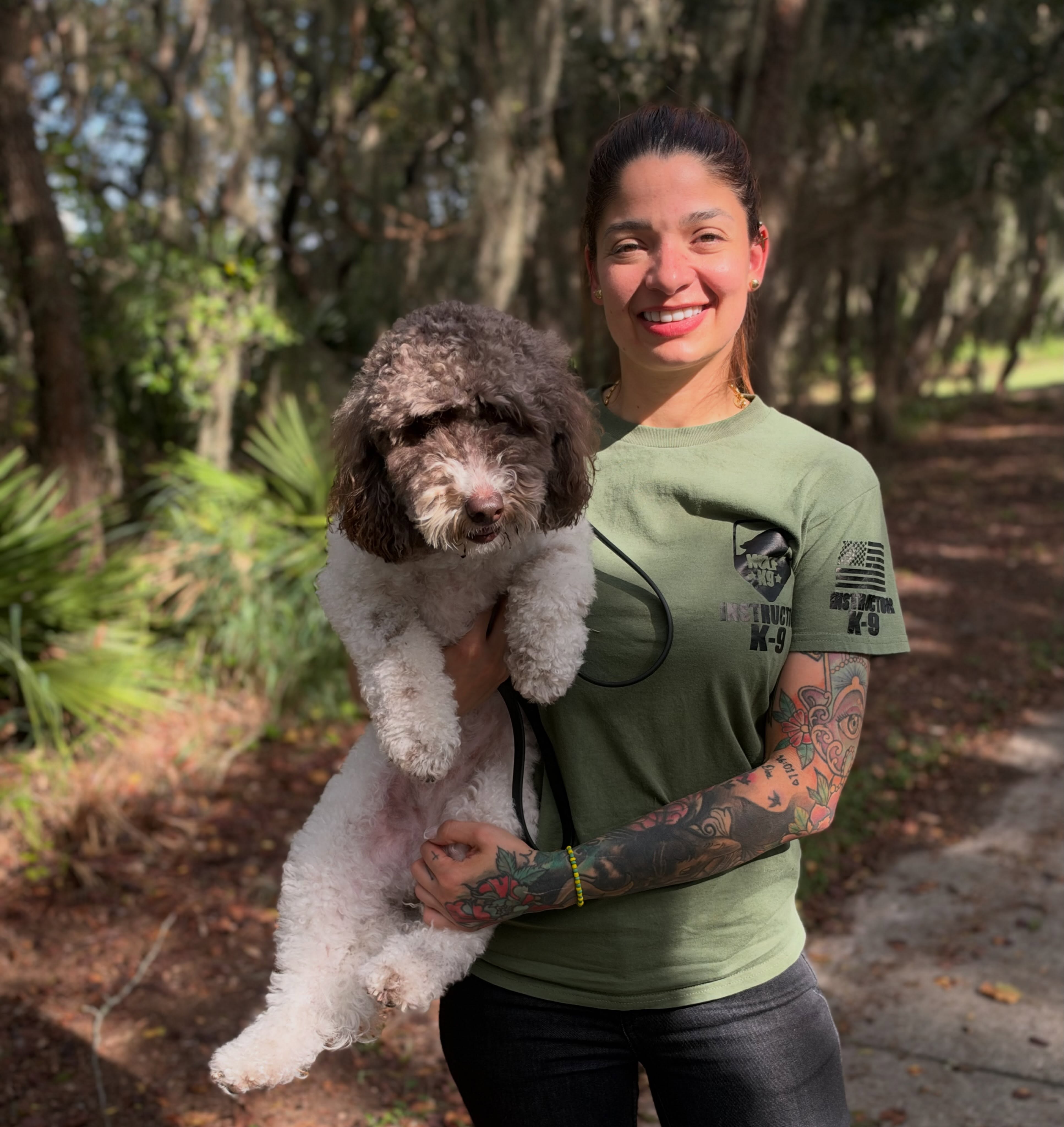 Entrenadora abrazando a Cookie, una goldendoodle, bajo los árboles